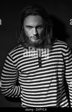 Un uomo in perline, capelli lunghi, modello maschile, in posa di una camicia striscia. Un buio in bianco e nero la moda maschile ritratto Foto Stock