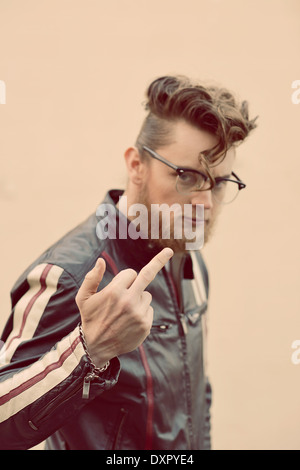 Un uomo barbuto in pompadour vintage pettinatura e occhiali vintage flipping il suo dito medio, un tagliente ritratto vintage concept Foto Stock