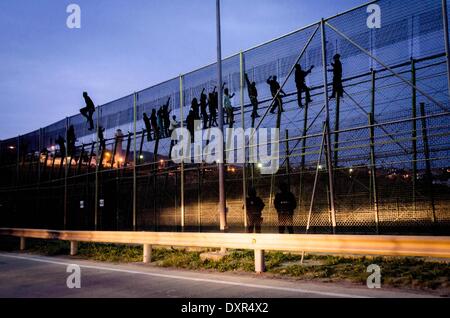 Melilla, Spagna. 28 Mar, 2014. I migranti subsahariana scavalcare una recinzione metallica che divide il Marocco e le enclave spagnola di Melilla venerdì 28 marzo 2014. Hanno detto i funzionari di diverse centinaia di migranti africani ha cercato di attraversare frontiera di filo spinato recinzioni per inserire l'enclave spagnola di Melilla dal Marocco ma la maggior parte sono state nuovamente girata da parte delle forze di sicurezza da entrambi i lati. Un Ministero degli Interni portavoce di Melilla detta i migranti hanno tentato di scalare le recinzioni diverse volte primi Venerdì e una manciata è riuscito a ottenere in tutta. Migliaia di migranti in cerca di una vita migliore in Europa vivono illegalmente in Foto Stock