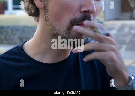 Un giovane uomo di fumare una sigaretta marihuana in strada a Santa Ana, Costa Rica Foto Stock