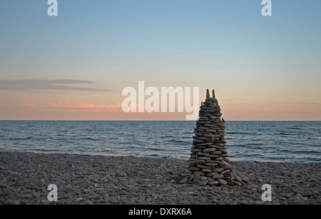 La piramide di pietre sulla spiaggia durante il tramonto Foto Stock