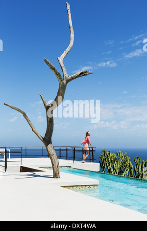 Donna in piedi sul bordo della piscina balcone con vista oceano Foto Stock