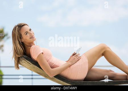 Ritratto di donna sorridente con tavoletta digitale sulla sedia a sdraio Foto Stock