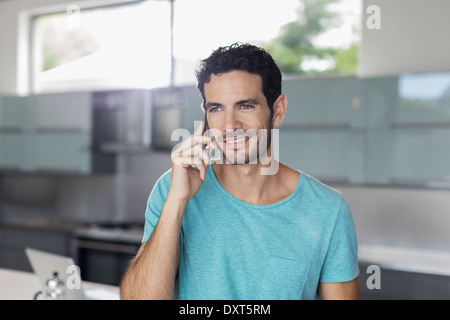 Uomo sorridente parlando al cellulare in cucina Foto Stock