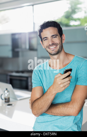 Ritratto di uomo sorridente con un telefono cellulare in cucina Foto Stock