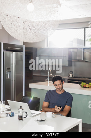 L'uomo texting con un telefono cellulare al tavolo della cucina Foto Stock