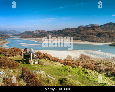 Un pensionato giovane seduto su una panchina in corrispondenza di un punto di vista sulla passeggiata panoramica che si affaccia sulla Mawddach estuary e Cadair Idris gamma. Foto Stock