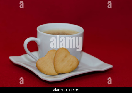 Tazza da caffè e due a forma di cuore i cookie su sfondo rosso con copia spazio. Foto Stock