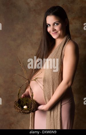 Giovane donna incinta tenendo un nido con un uovo Foto Stock