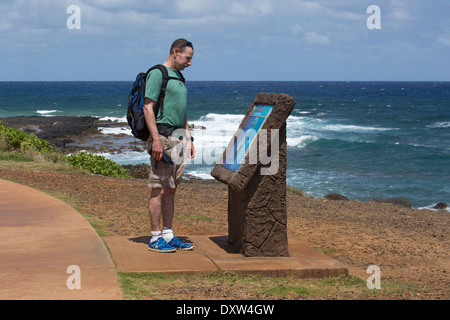 Fit senior man leggere il segno interpretativo mentre si cammina sul percorso Kauai condiviso, Ke Ala Hele Makalae, lungo la costa oceanica delle Hawaii. (età 60) Foto Stock