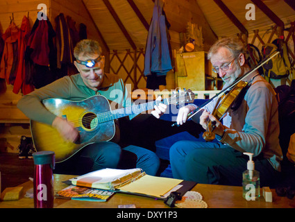 Maschio di musicisti di suonare il violino e chitarra in remoto paese indietro yurt, North Cascade Mountains, nello stato di Washington, USA Foto Stock