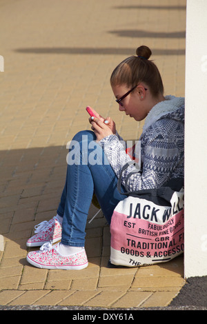 Ragazza seduta sul terreno texting sul telefono a Bournemouth in Marzo Foto Stock