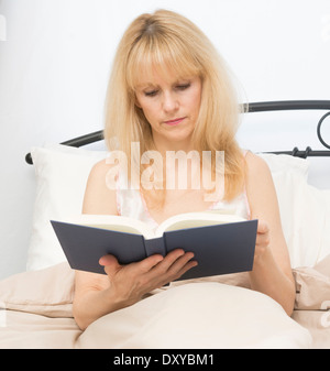 La mezza età della donna nel letto la lettura di un libro Foto Stock