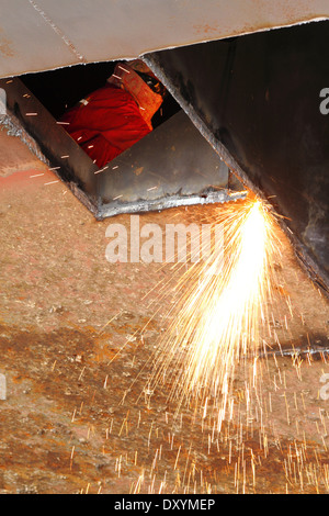 Le scintille volano come acciaio viene tagliata da un vecchio chiatta da un ossi-acetilene torcia presso un cantiere in Malaysia. Foto Stock