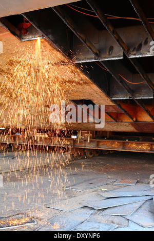 Le scintille volano come acciaio viene tagliata da un vecchio chiatta da un ossi-acetilene torcia presso un cantiere in Malaysia. Foto Stock