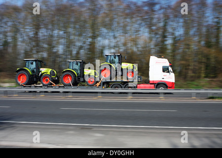 Un MDF articolato di trasporto caricatore basso portante tre trattori lungo la A12 in Essex, Inghilterra Foto Stock