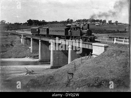 Questa fotografia, scattata intorno al 1930, mostra un motore a cisterna di classe 20 che tira un treno passeggeri suburbano a Camden, nel nuovo Galles del Sud. Il treno presenta una carrozza e un pullman per il lavoro, tipico dei treni passeggeri dell'epoca. L'immagine evidenzia l'importanza del treno a vapore per il trasporto all'inizio del XX secolo. Foto Stock