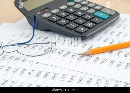 Calcolatrice con matita e occhiali su dati finanziari sulla scrivania Foto Stock