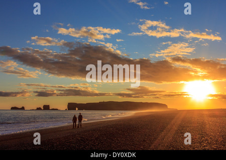 Coppia a piedi lungo la spiaggia di Reynisfjara al tramonto Foto Stock