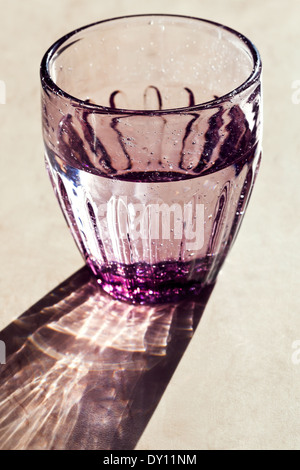Viola sfaccettata in vetro con acqua potabile illuminata dalla luce del sole Foto Stock