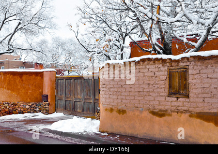 Un inverno di scena di neve dispone di vecchi e nuovi muri e il cancello di legno nella struttura ad albero laden Canyon Road area di Santa Fe, NM Foto Stock