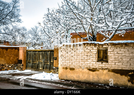 Un inverno di scena di neve dispone di vecchi e nuovi muri e il cancello di legno nella struttura ad albero laden Canyon Road area di Santa Fe, NM Foto Stock