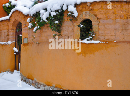 Una scena di neve offre affascinanti parete adobe con il cancello che conduce al cortile nel Canyon storica area di strada di Santa Fe, NM Foto Stock