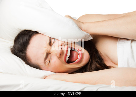 Un frustrato stanco donna si nasconde la sua testa nel suo cuscino e urla perché lei non riesce a dormire. Isolato su bianco. Foto Stock