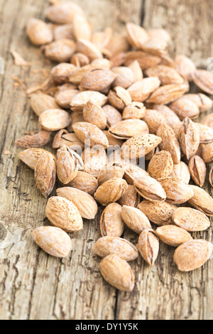 Arrosto di mandorle salate nel loro guscio, sparsi in legno rustico board. Foto Stock