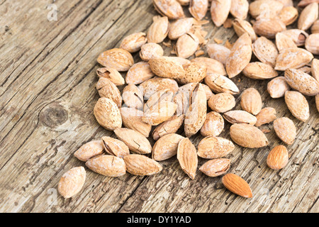 Arrosto di mandorle salate nel loro guscio, sparsi in legno rustico board. Foto Stock