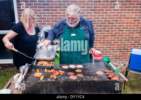 Un uomo e una donna cucinare la carne su un carbone barbeque all'aperto presso un estate fete. Foto Stock