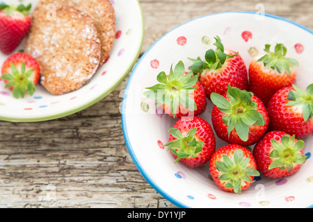 Intero fragole spagnole in una ceramica ciotola rustico, posto sulla tavola in legno rustico con fatti in casa nocciola cookies. Foto Stock