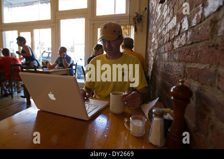 Uomo in occupato cafè usa il computer portatile mentre si beve il caffè Foto Stock