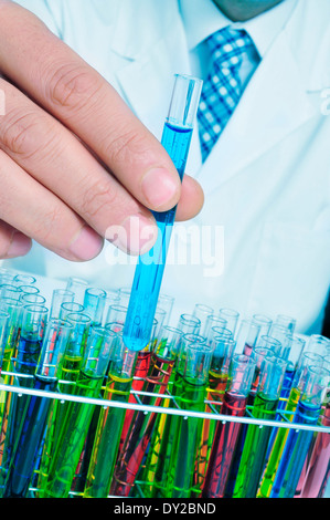 Uomo in camice bianco con provette con liquidi di colori differenti in un laboratorio Foto Stock