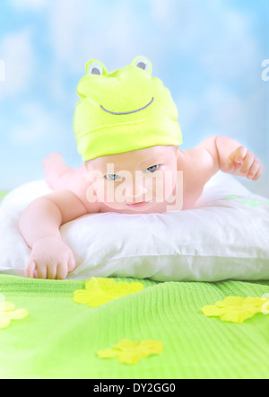 Closeup ritratto di carino piccolo bambino indossando funny frog costume e sdraiarsi a immaginare campo floreale in casa, infanzia felice Foto Stock