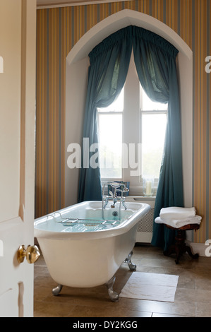 Free standing roll top bagno in bagno con carta da parati a strisce e teal tende Foto Stock