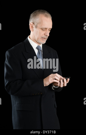 Imprenditore Senior in abito nero la scrittura di sms o comporre un numero sul suo telefono cellulare, su sfondo nero Foto Stock