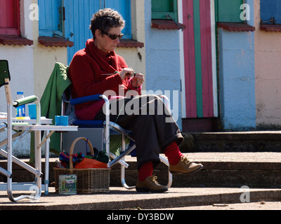 Donna anziana seduto di fronte spiaggia capanne maglia, Crooklets Beach, Bude, Cornwall, Regno Unito Foto Stock