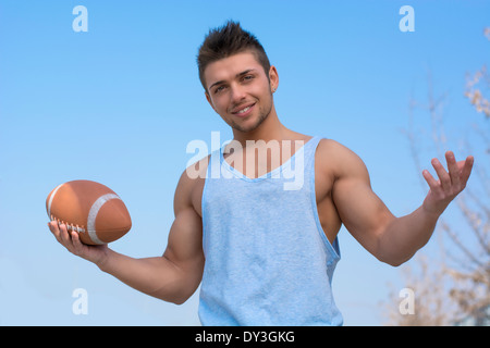 Muscolare di giocatore di football americano in piedi con la palla in mano, i bracci aperti sorridente. Colpo all'aperto Foto Stock