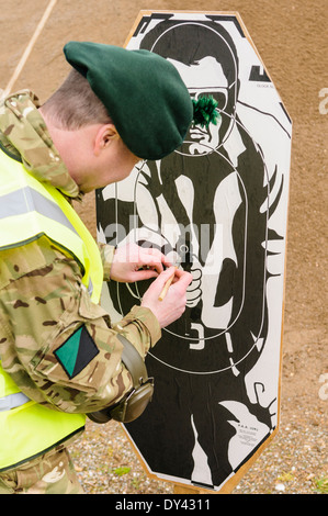 Un soldato dal Royal Irish Regiment ripara un target utilizzando la colla e la carta dopo la ripresa Foto Stock