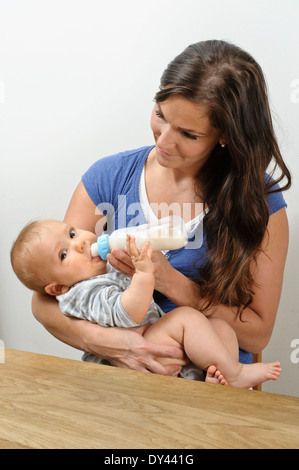 Feed madre di sette mesi con bottiglia di latte. Ella culle il bambino nelle braccia Foto Stock