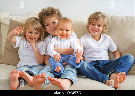 Quattro fratelli, giovani ragazzi, seduto su un divano. Il primogenito è in possesso di un bambino in grembo. Essi stanno cercando di sinistra della videocamera Foto Stock