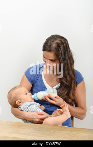 Feed madre di sette mesi con bottiglia di latte. Ella culle il bambino nelle braccia Foto Stock