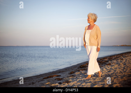 Ritratto di una donna matura di camminare sulla spiaggia guardando il mare. Rilassata old Lady per passeggiare sulla spiaggia con copia spazio. Foto Stock