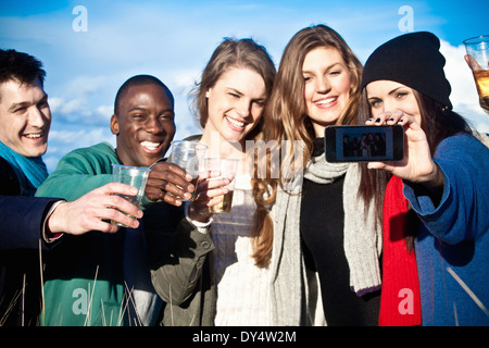 Giovani amici adulti la tostatura con vino bianco e tenendo selfie Foto Stock