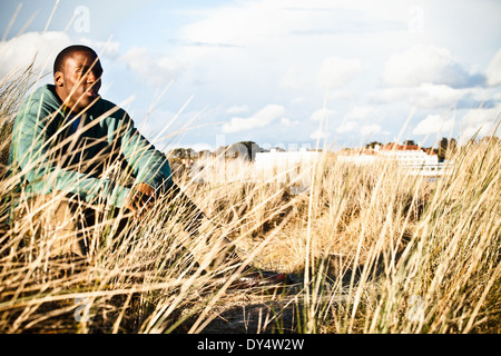 Giovane uomo seduto in dune di sabbia, Bournemouth Dorset, Regno Unito Foto Stock