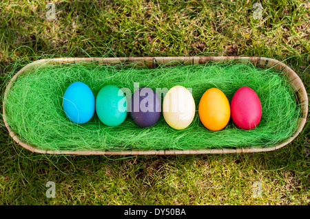 Colore diverso le uova di Pasqua in un cesto su un'erba Foto Stock