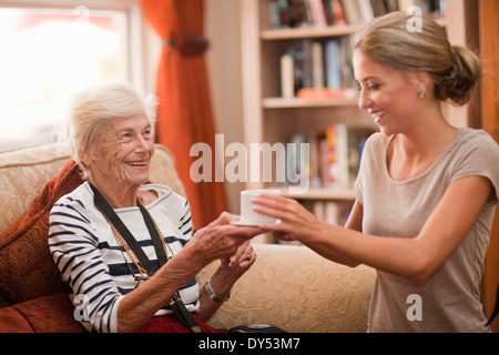 Care Assistant consegna tazza da caffè per senior donna Foto Stock