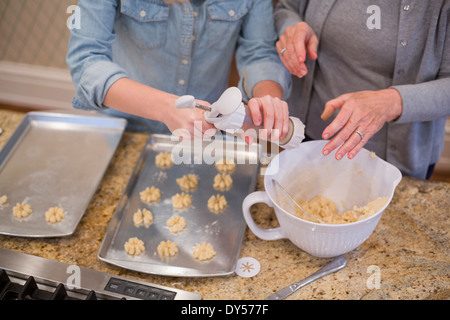 Donna Senior e nipote di biscotti di tubazioni sul vassoio da forno Foto Stock