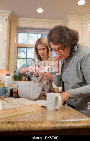 Donna Senior e nipote versando la cottura in cucina Foto Stock